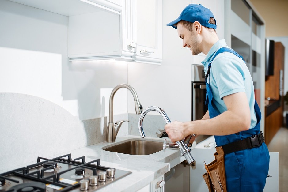 Plumber In Uniform Changes Faucet In The Kitchen